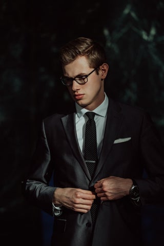 Model wearing a tailored dark suit, black tie, and white dress shirt.