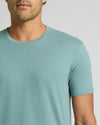 A close-up of a man wearing a short-sleeve crew-neck t-shirt in a light teal blue color, shown from the chin down against a neutral light gray background.