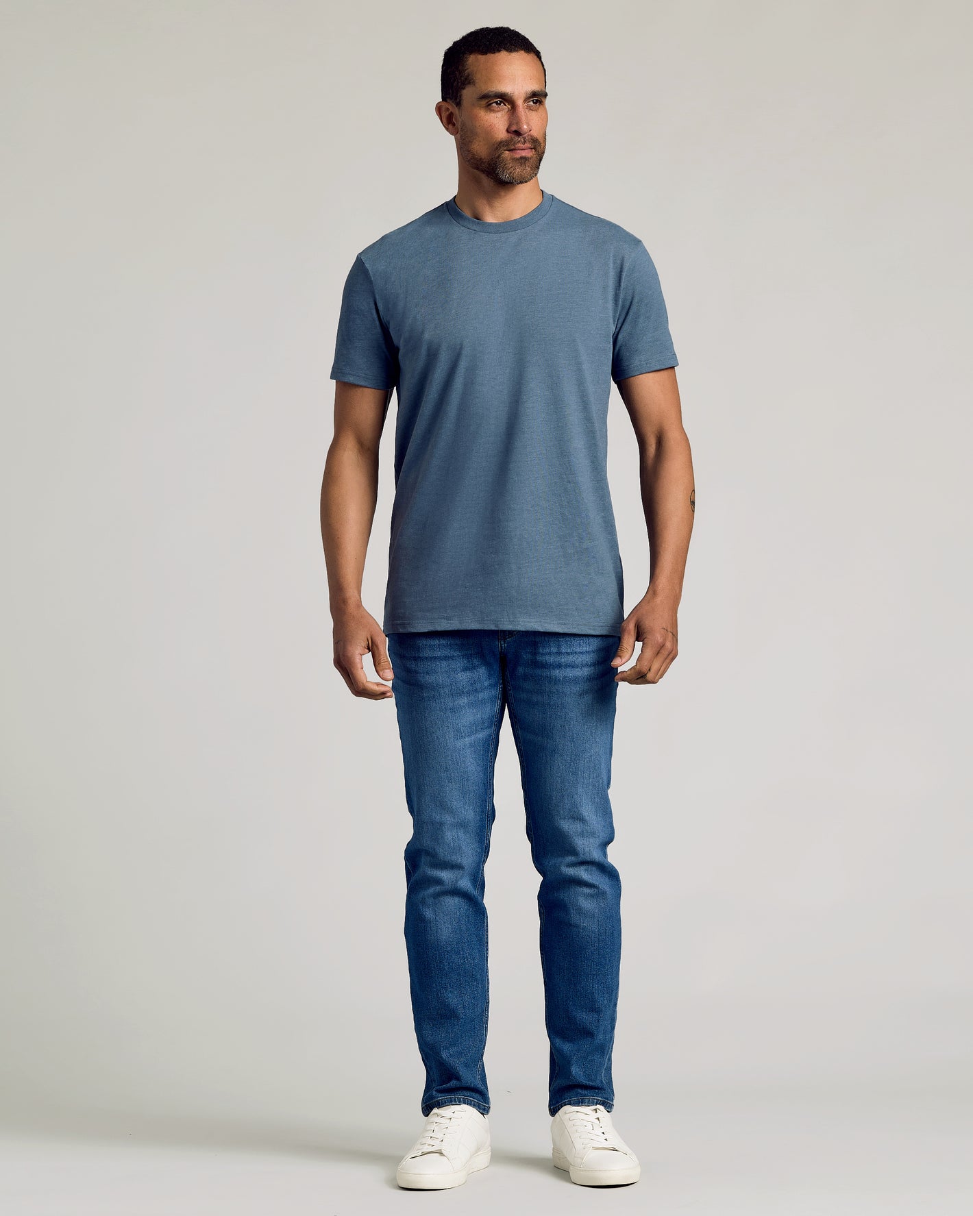 Man wears Dark Heather Tempest Classic Crew Neck and slim-fit jeans.
