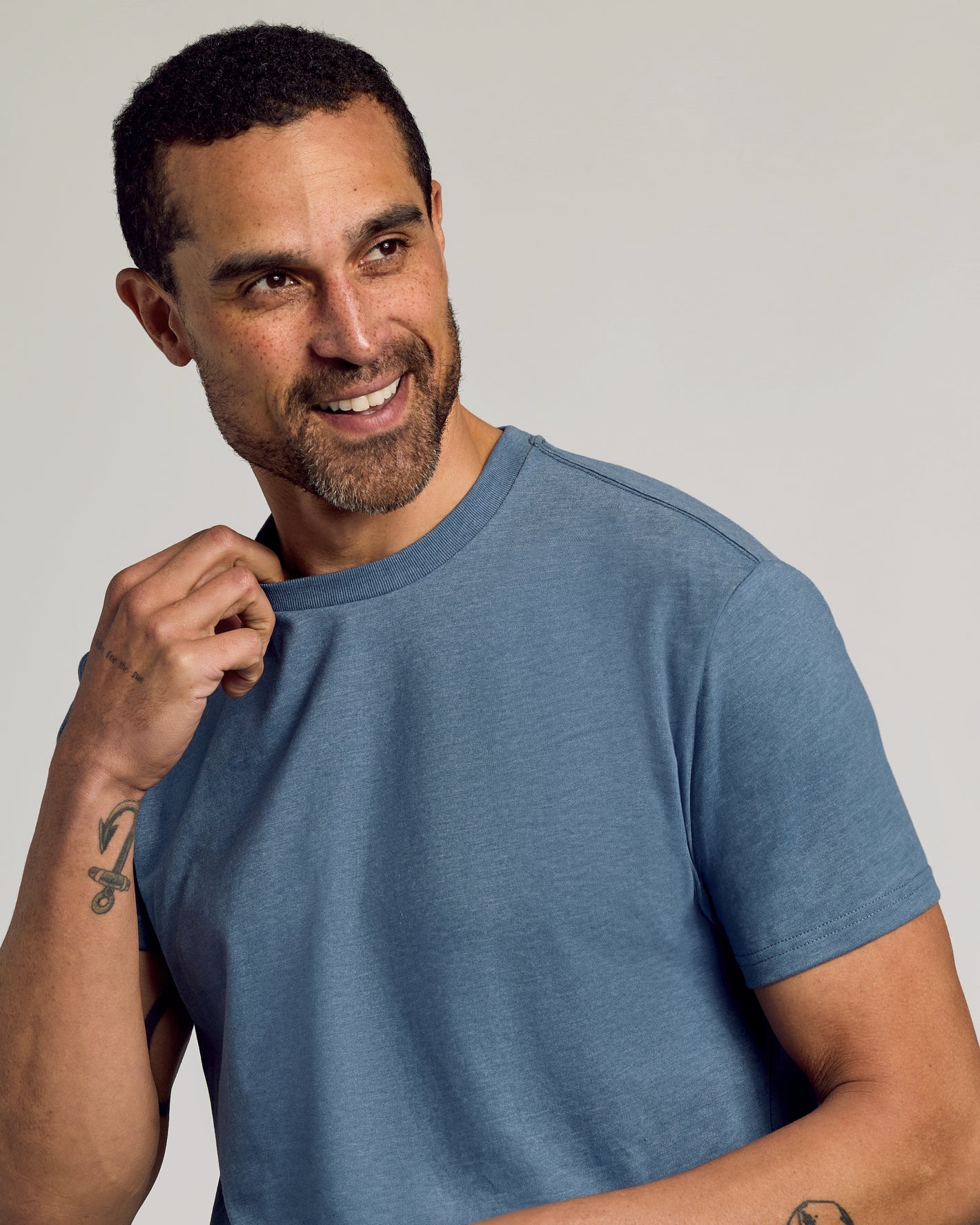 Man wearing Dark Heather Tempest Classic Crew Neck, smiling, showcasing tattoos.