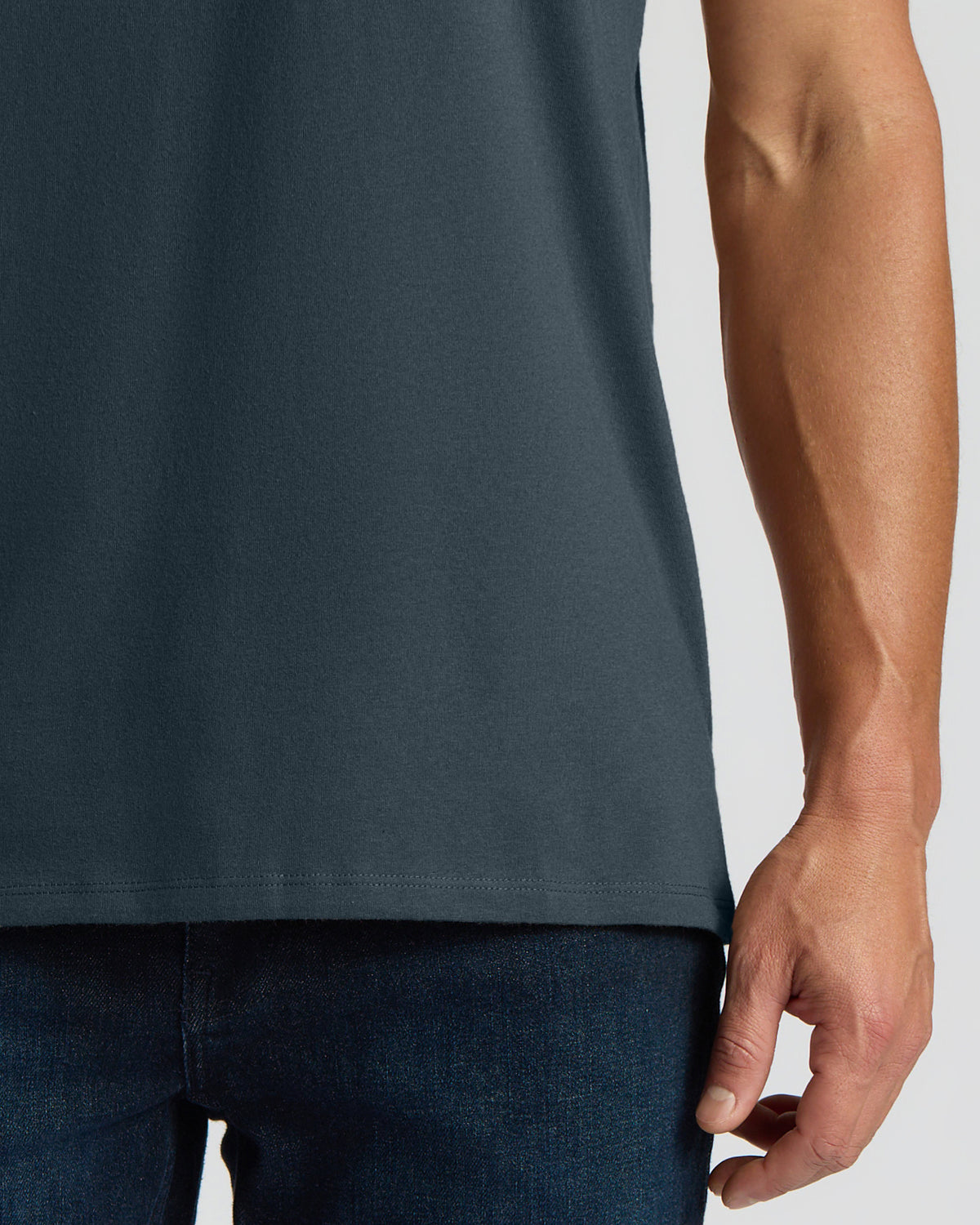 Close-up of a person wearing a dark slate blue-gray t-shirt and dark blue jeans, showing the side profile and hand against a light gray background.