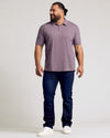 Man wearing Dark Heather Amethyst Short Sleeve Polo, dark jeans, white sneakers.