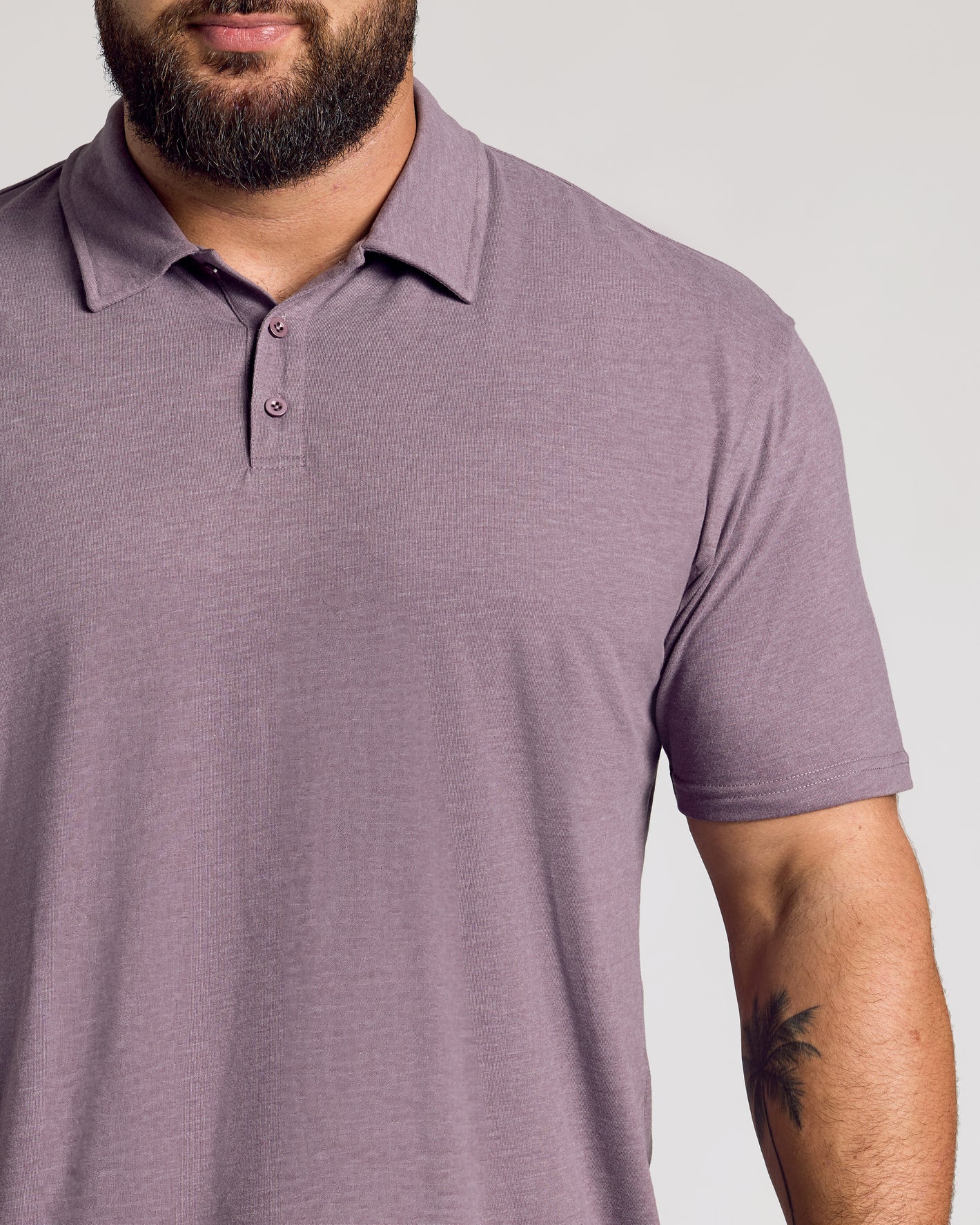 Man wearing Dark Heather Amethyst Short Sleeve Polo with palm tree tattoo.