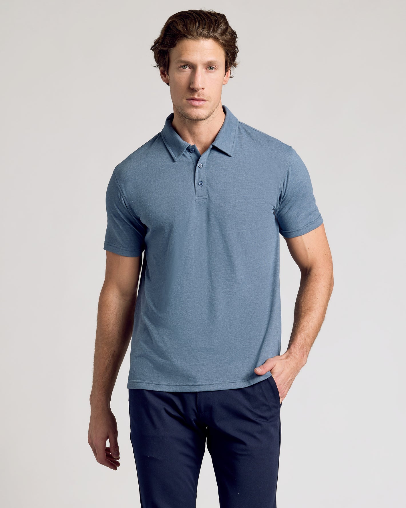 Man wearing Dark Heather Tempest Short Sleeve Polo with navy trousers.
