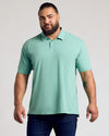 Man in Light Heather Greenery Classic Polo with palm tree tattoo.