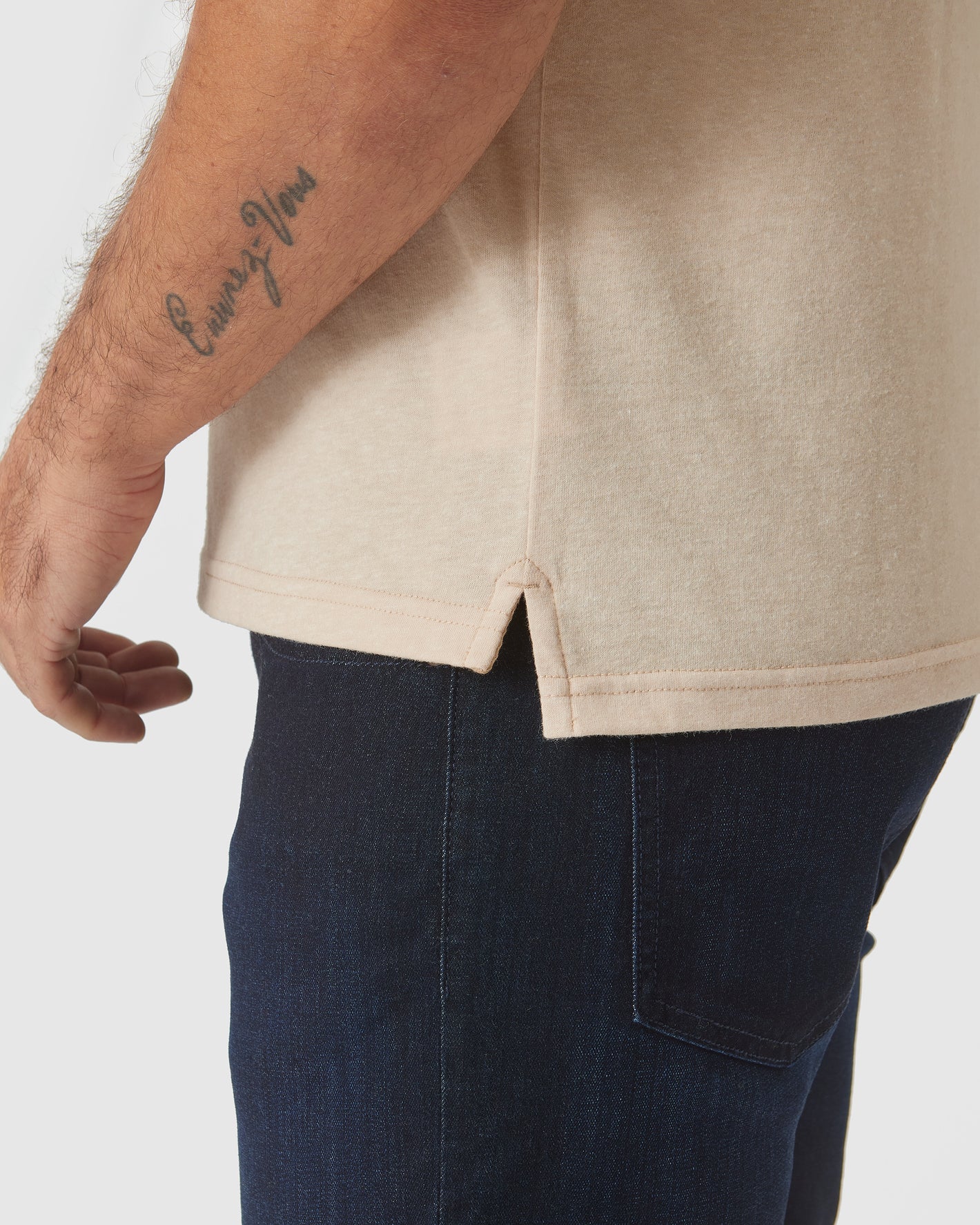Light Camel Cream Heather Polo with side-slit hem and forearm tattoo visible.