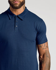 True ClassicA close-up of a man wearing a navy blue short-sleeve polo shirt against a light gray background.