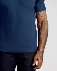 True ClassicA close-up of a person wearing a solid navy blue short-sleeve t-shirt and dark pants, showing the side of the torso and tattooed arm against a light gray background.