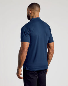 True ClassicA man viewed from the back wearing a navy blue short-sleeve polo shirt and dark trousers, standing against a plain light gray studio background.