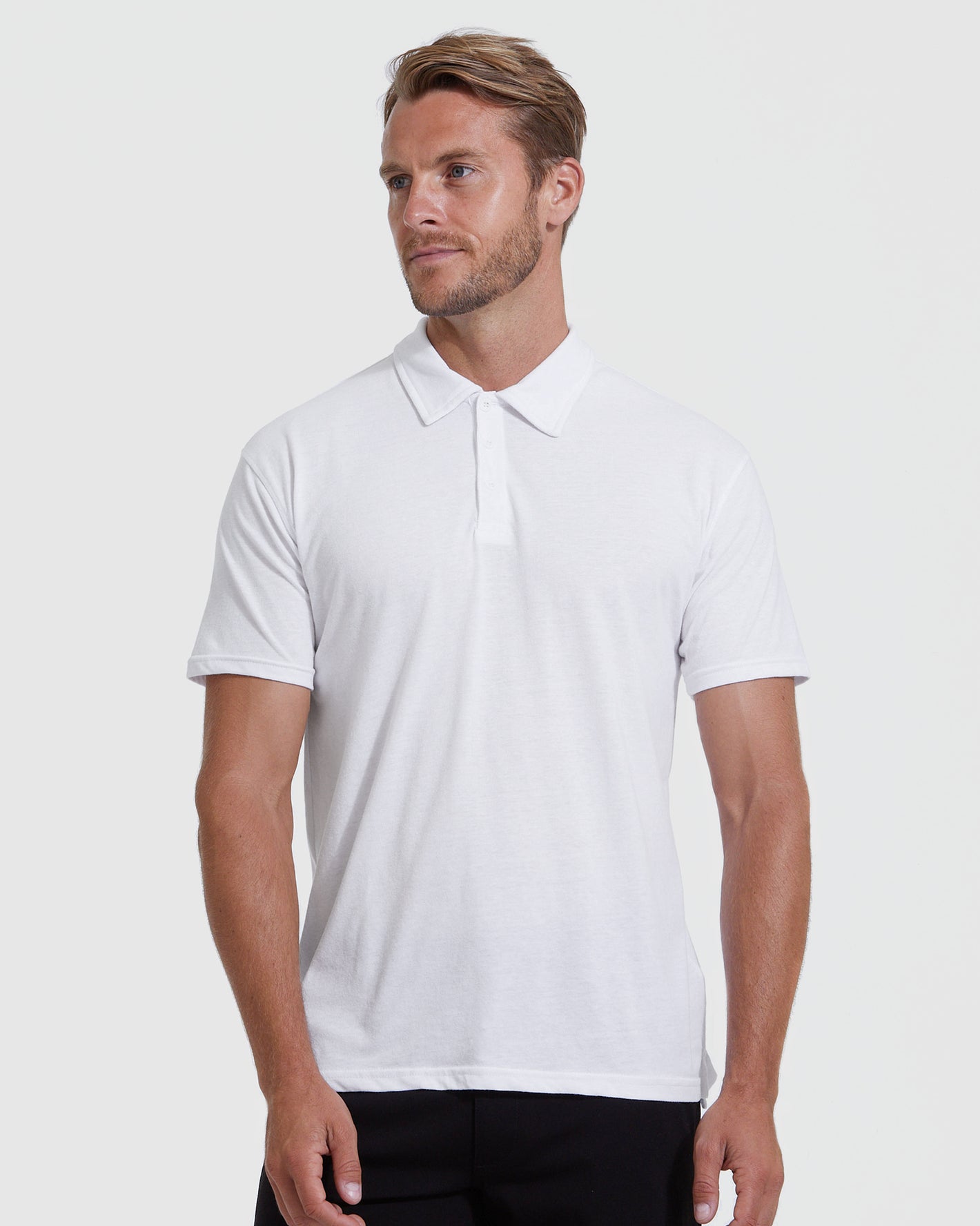 Man in White Classic Polo 6-Pack, relaxed pose, gray background.