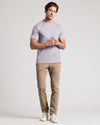 A man modeling a light lavender crew-neck t-shirt, khaki pants, and white sneakers against a plain light gray studio background.
