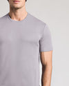A close-up of a man wearing a light gray crew-neck t-shirt against a neutral light gray background.