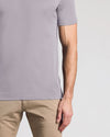 A close-up of a man wearing a light gray short-sleeve t-shirt and khaki pants, cropped from the chest down against a light gray background.
