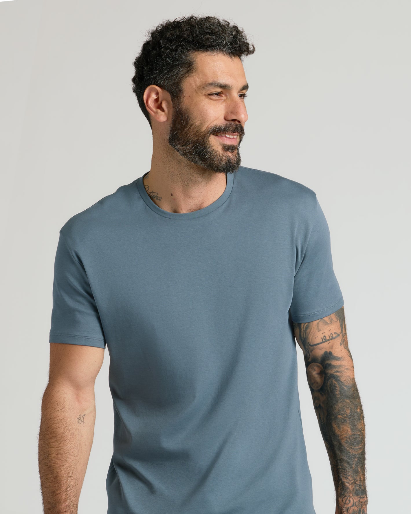 Man wearing Tempest Premium Pima Crew Neck, showcasing tattoos, slight smile.