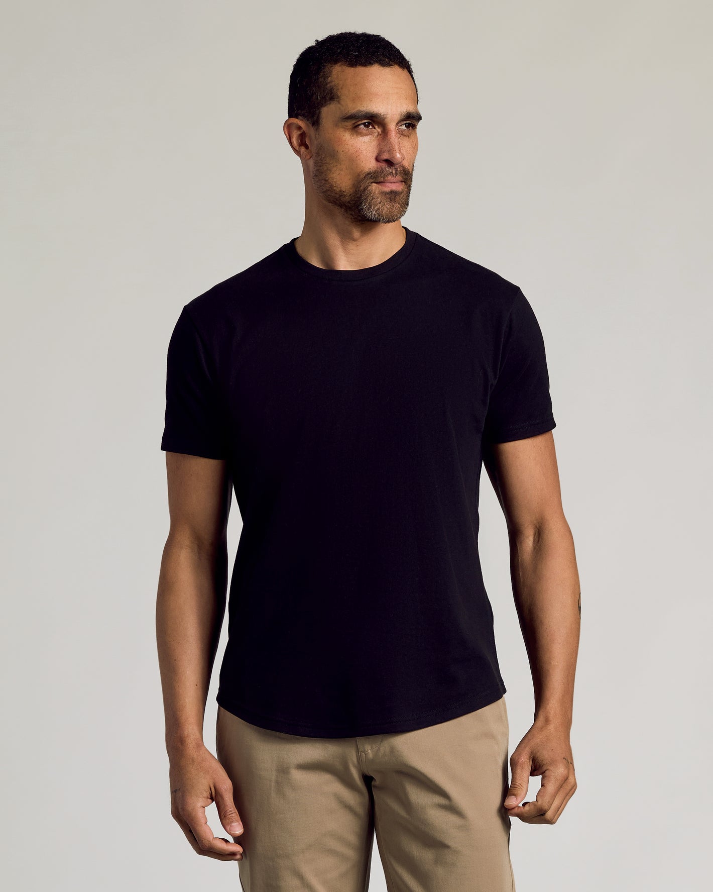 Man wearing Black Curved Hem Classic Crew Neck T-shirt with tan trousers.