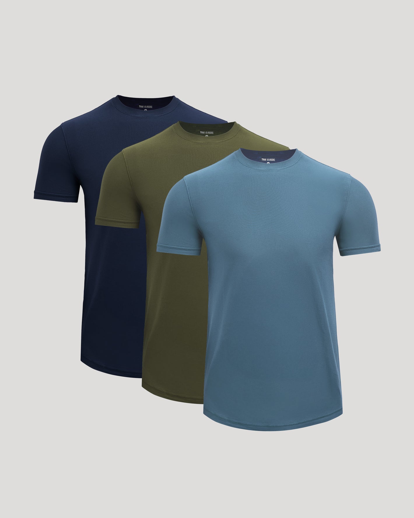Three short-sleeve crew-neck t-shirts in navy blue, olive green, and slate blue, arranged in a staggered overlapping display on a light gray background.