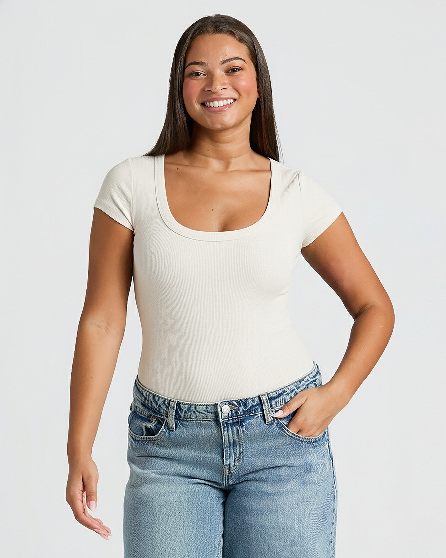 Woman wearing a white t-shirt and blue jeans against a plain background. MODEL_INFO: Jade is 5'9", wearing a size L