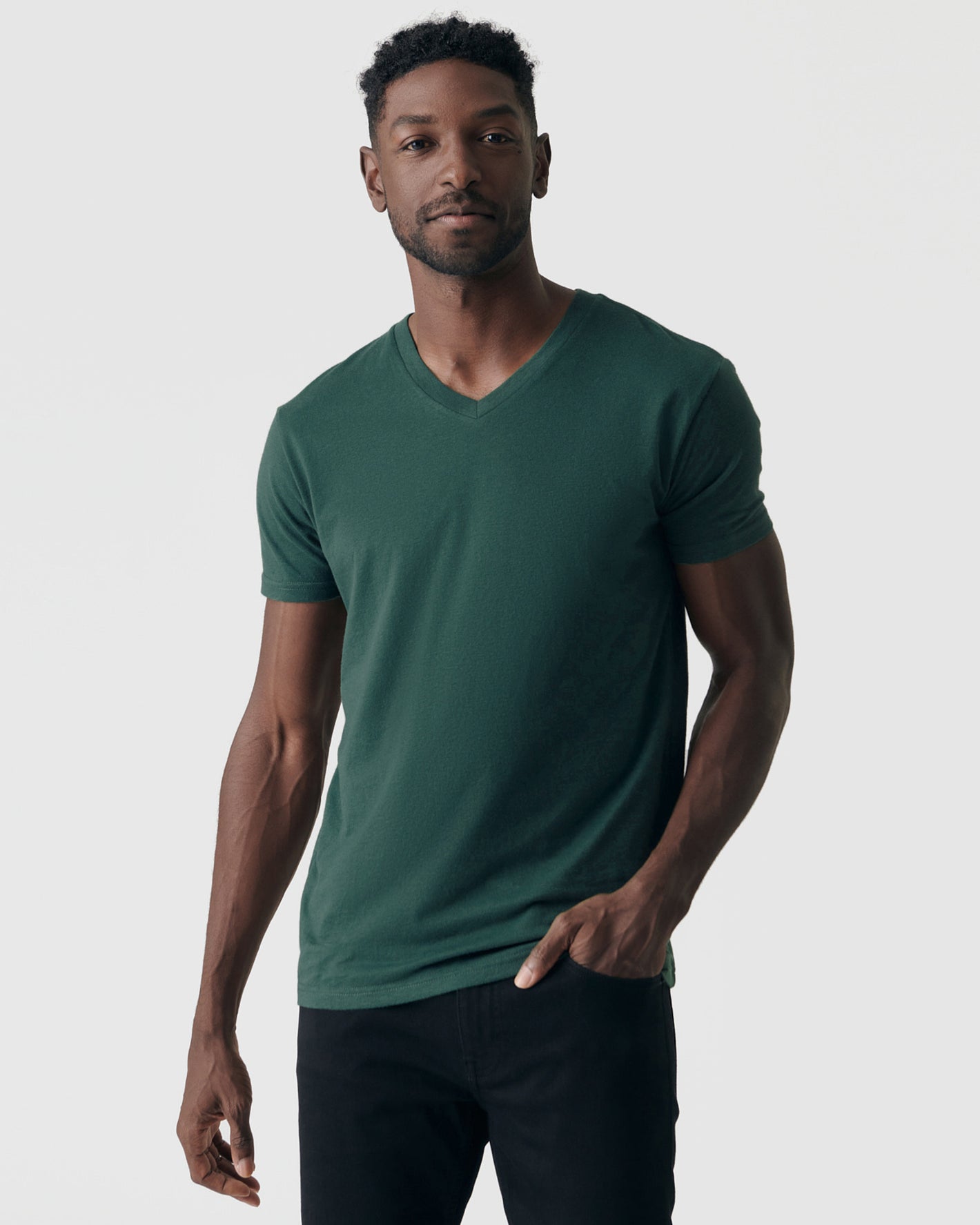 Man wearing Forest Green V-Neck Tee and dark trousers, standing casually.