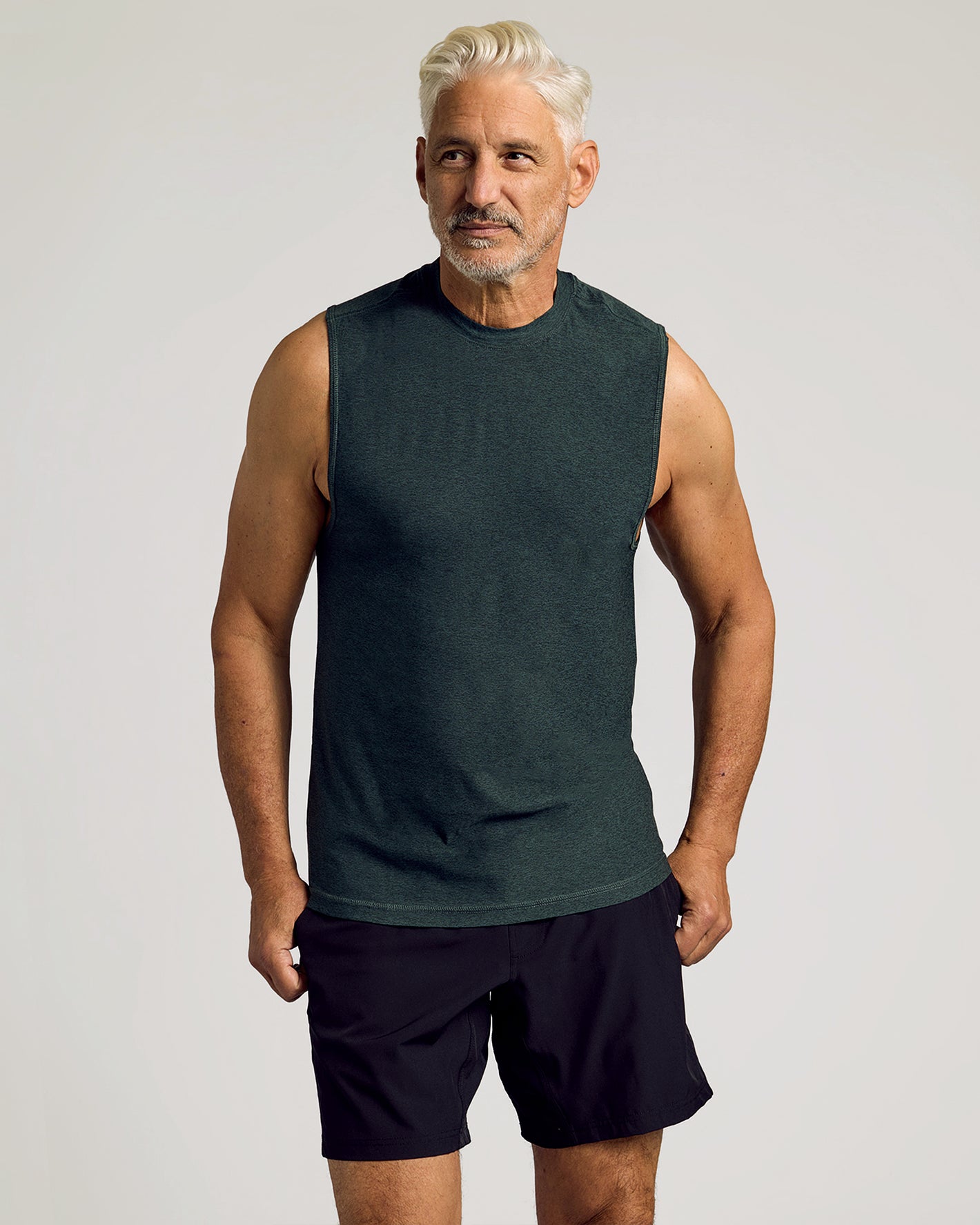Man in Dark Heather Forest Sleeveless Active Muscle Tee and black shorts.