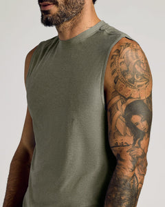 True ClassicClose-up of a man wearing a Heather Military Green Sleeveless Active Muscle Tee, showcasing the soft fabric and detailed tattoos on his arm in a casual setting.