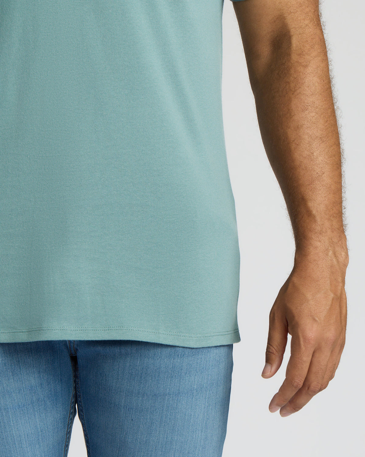 A close-up of a person wearing a light blue-green short-sleeve t-shirt and blue jeans against a plain light gray background.