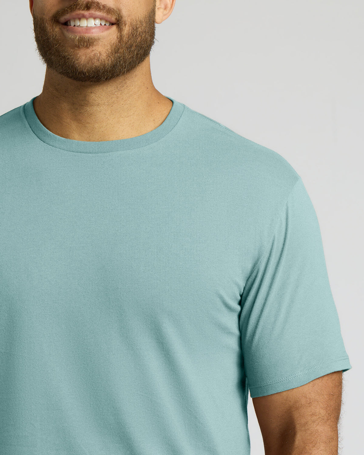 A close-up of a man wearing a light blue crew-neck t-shirt against a solid light gray background.