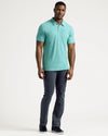 Man wears Light Heather Greenery Short Sleeve Tall Polo, slim charcoal pants.