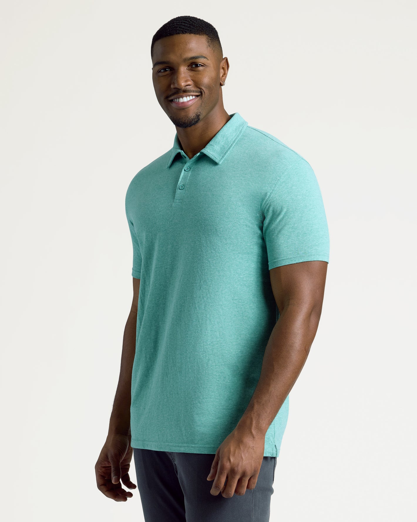 Young man wearing Light Heather Greenery Short Sleeve Tall Polo, smiling.