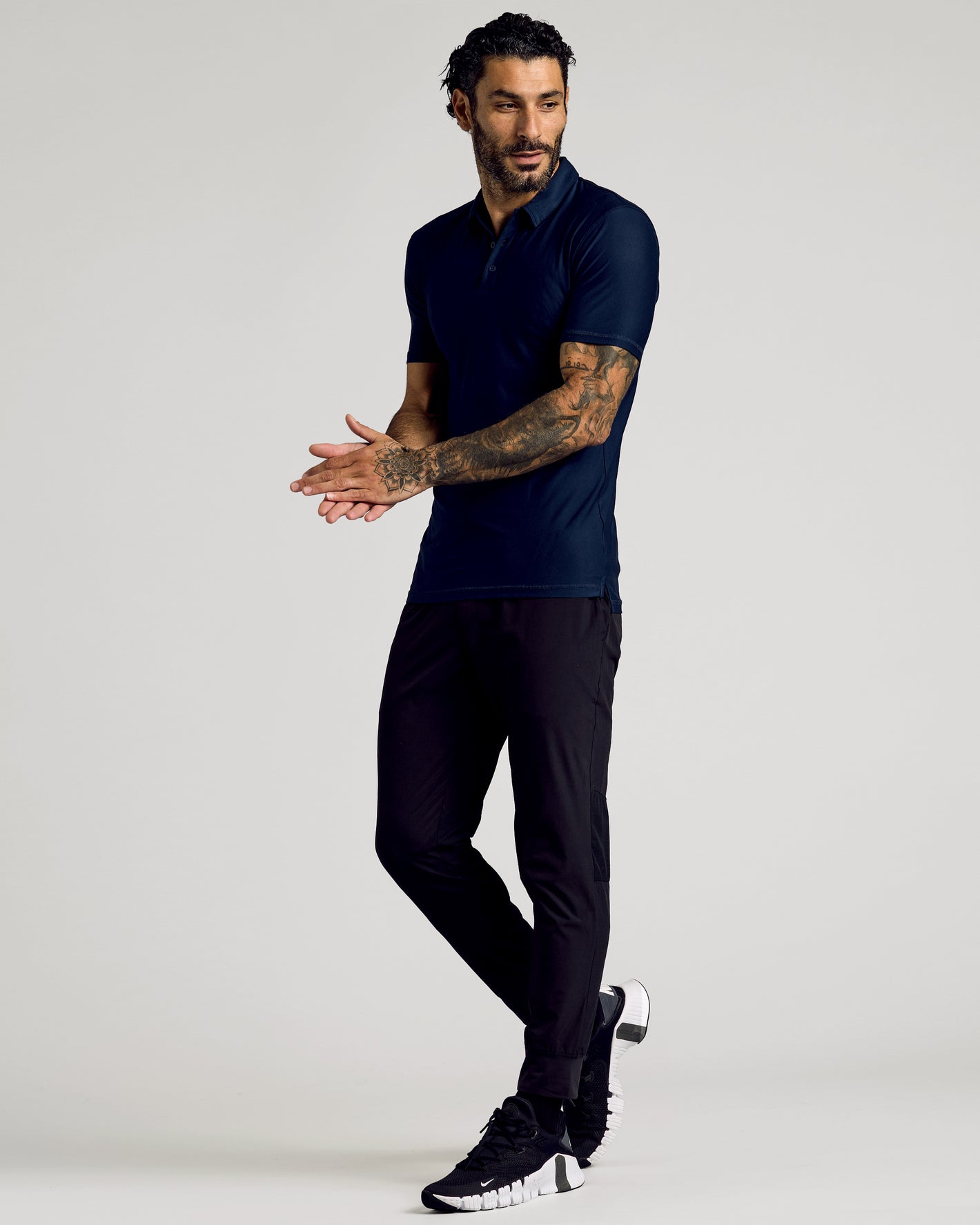 Man wearing Navy Short Sleeve Tall Active Polo, slim black joggers, athletic sneakers.
