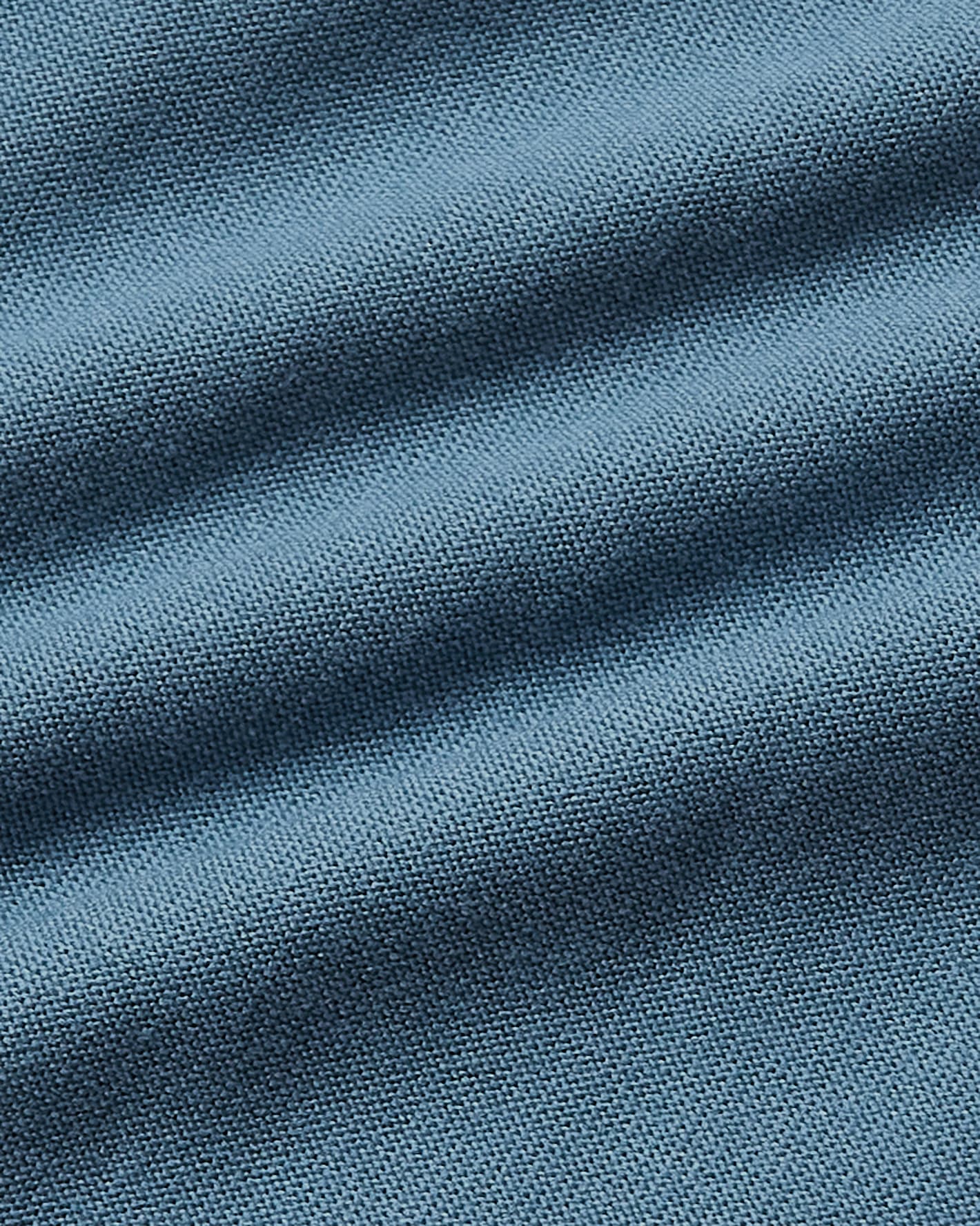 A close-up of textured blue fabric with soft diagonal folds and a fine woven pattern.