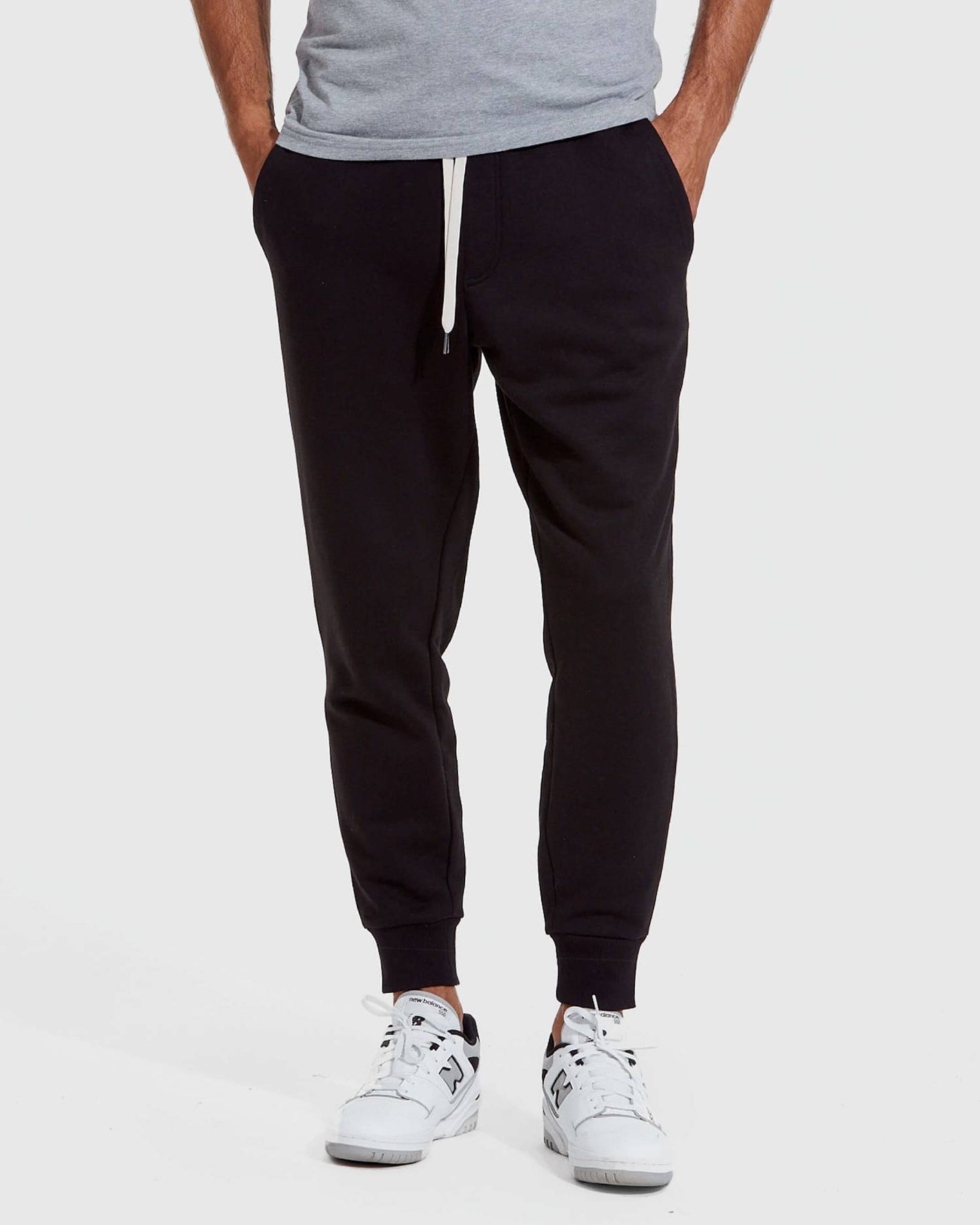Person wearing black jogger pants and white sneakers on a white background