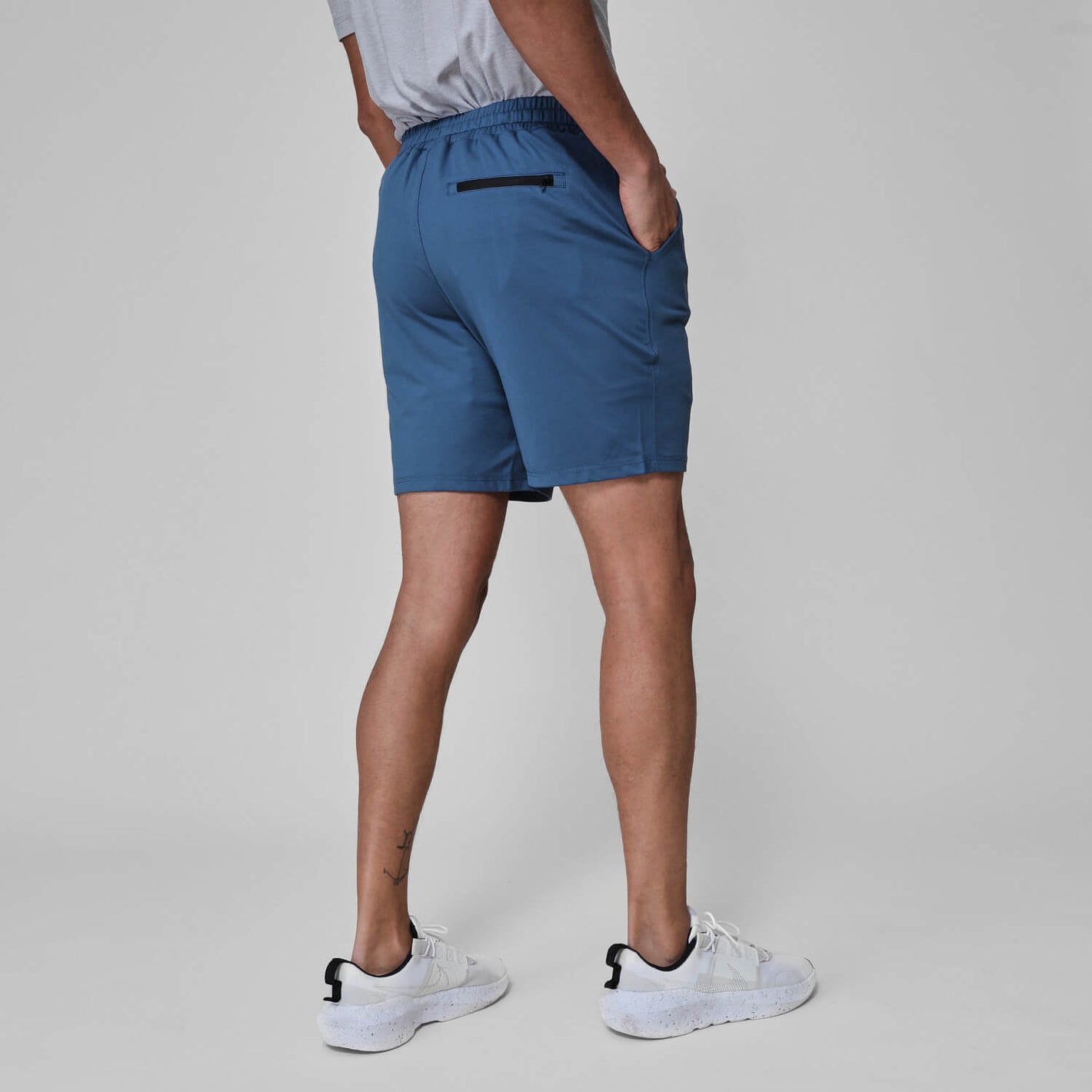 Person wearing Stone Blue Active Comfort Shorts, displaying back zip pocket and white sneakers.