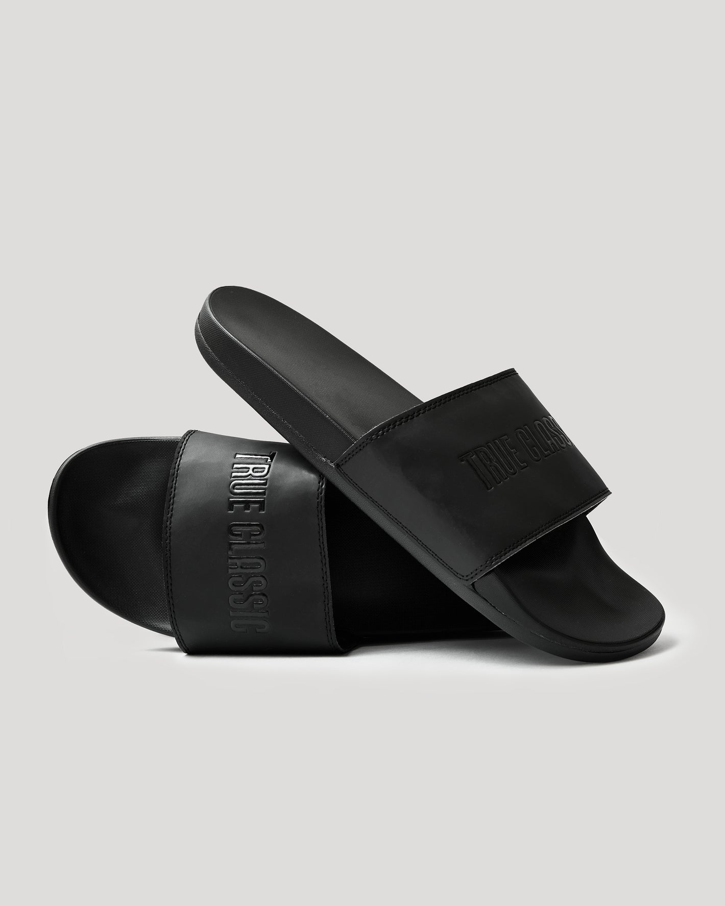 Black Comfort Slides with TRUE CLASSIC embossed on the strap, minimalist design.