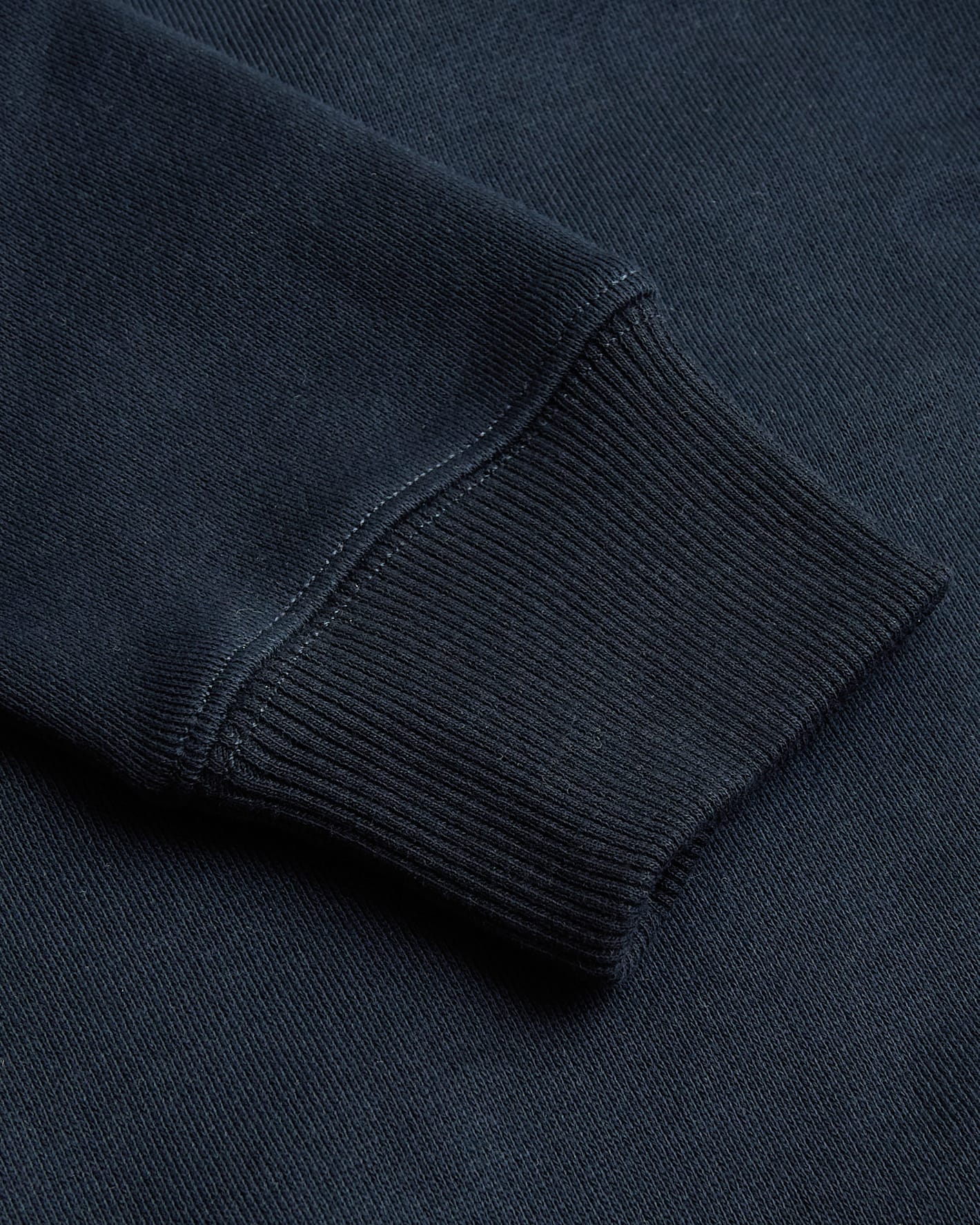 Close-up of a navy blue sweatshirt sleeve with ribbed texture.