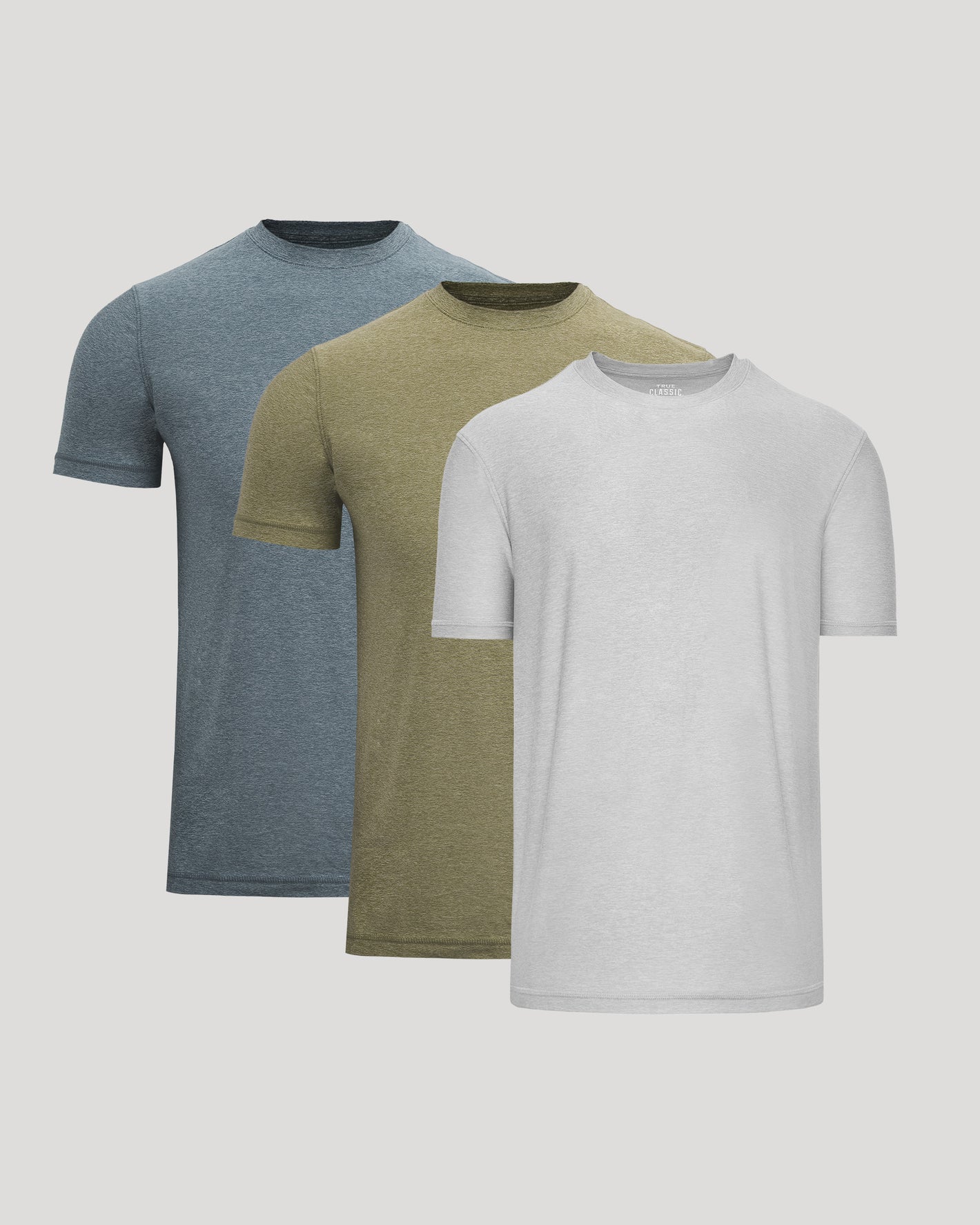 Three plain t-shirts in blue, green, and gray on a light gray background