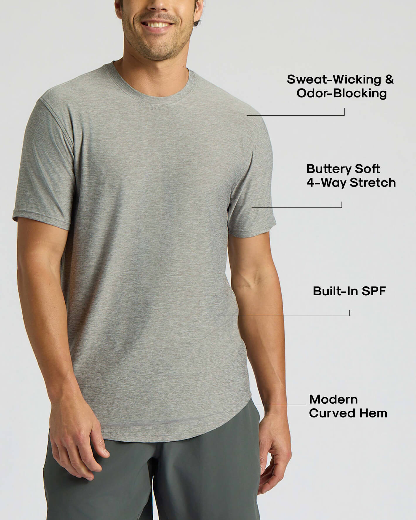 A man wearing a light gray heather short-sleeve athletic t-shirt with text callouts highlighting features like sweat-wicking, odor-blocking, 4-way stretch, built-in SPF, and curved hem.