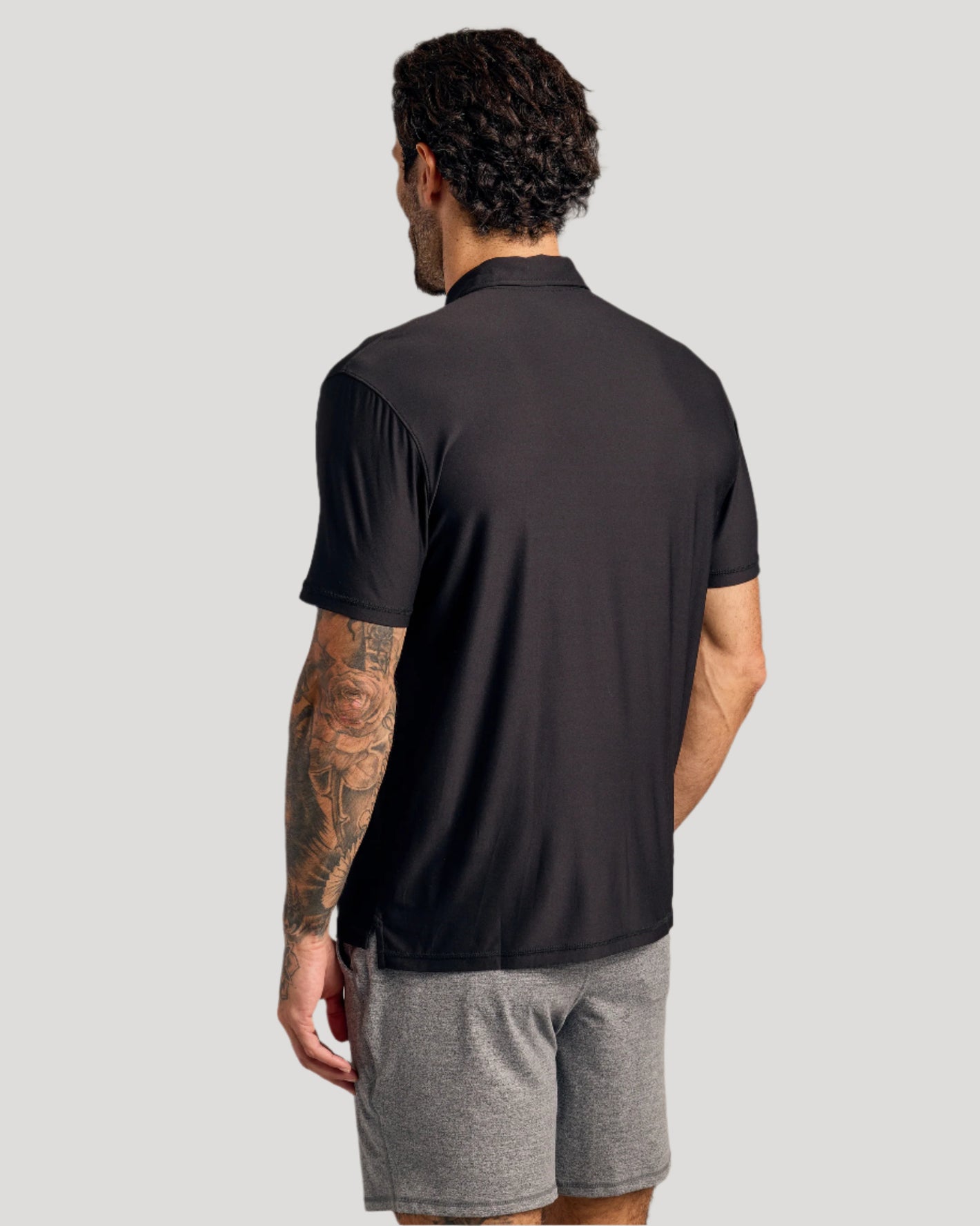 Man in Black Active Polo 3-Pack, showing back and tattooed arm.