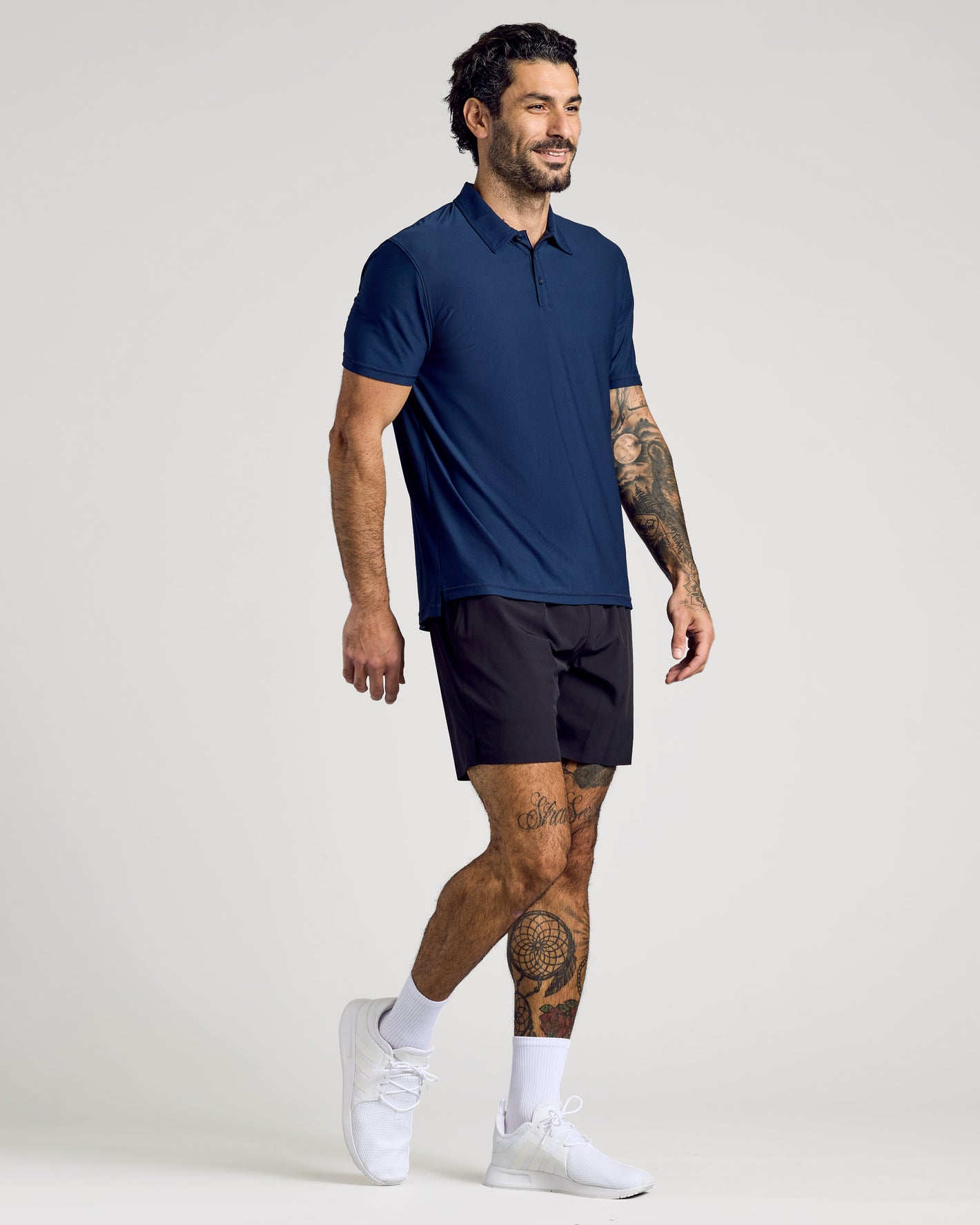 Model in Active Polo 6-Pack, navy polo, black shorts, walking.