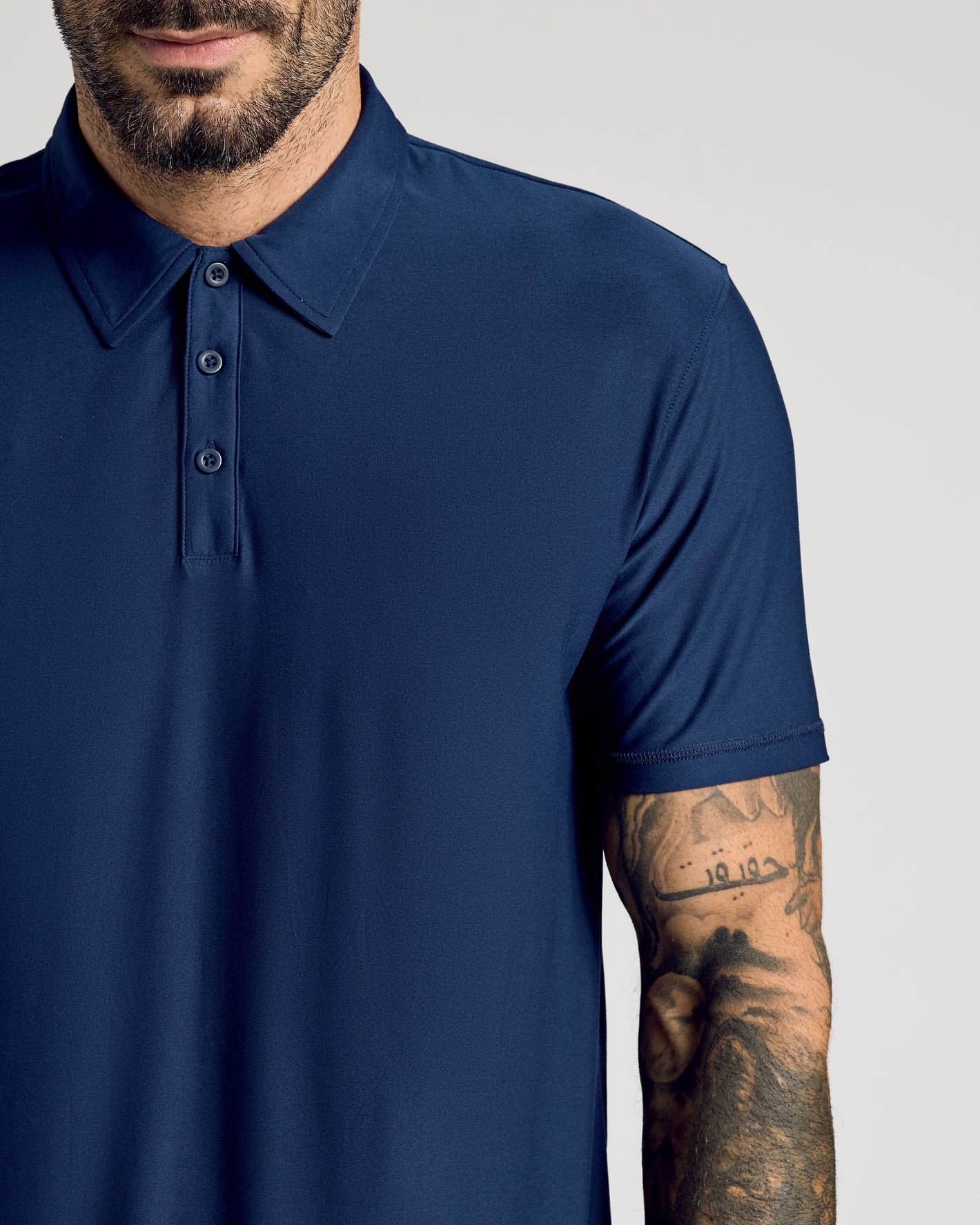 Man wearing navy Active Polo from 6-Pack collection, showcasing tattoos.