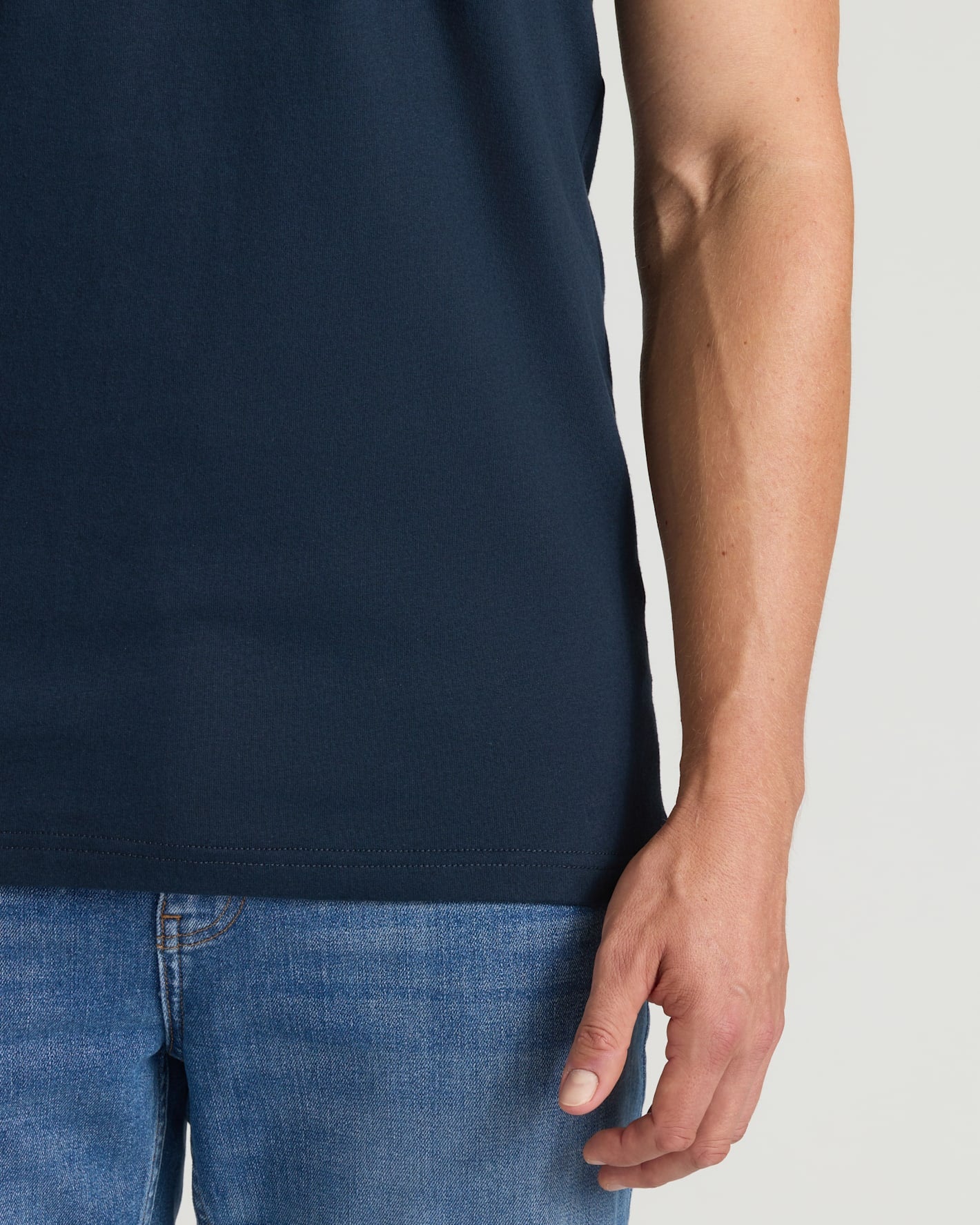 Person wearing a navy blue t-shirt and blue jeans on a light gray background