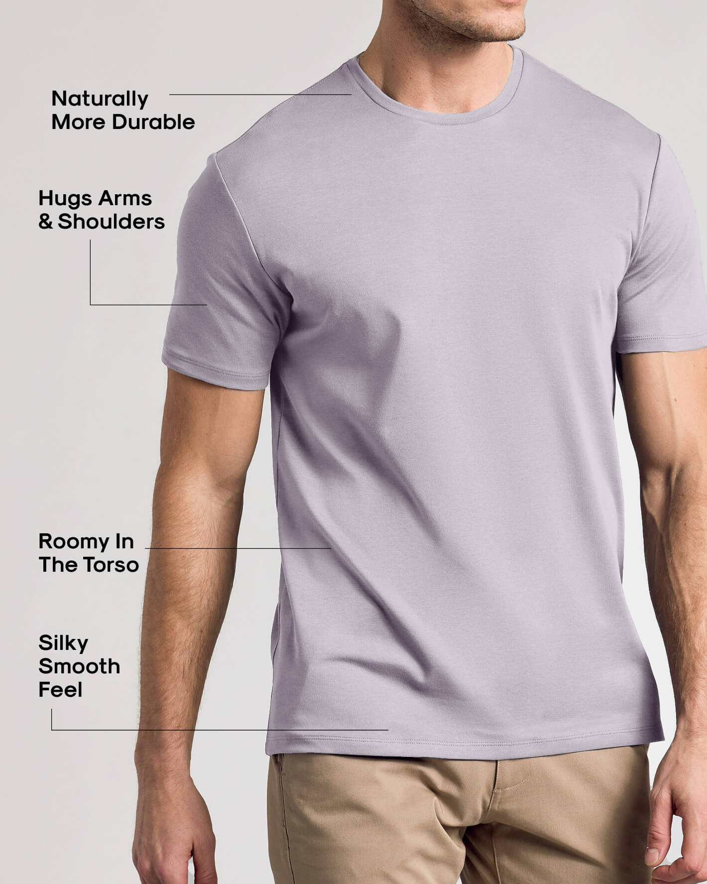 A man wearing a light lavender-gray short-sleeve crewneck t-shirt, with text callouts highlighting features like durability, arm fit, roominess in the torso, and smooth feel.