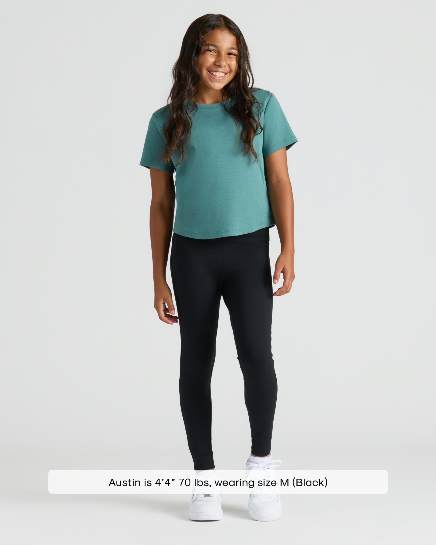 Child wearing Girls Black Foldover Leggings, teal T-shirt, and white sneakers.