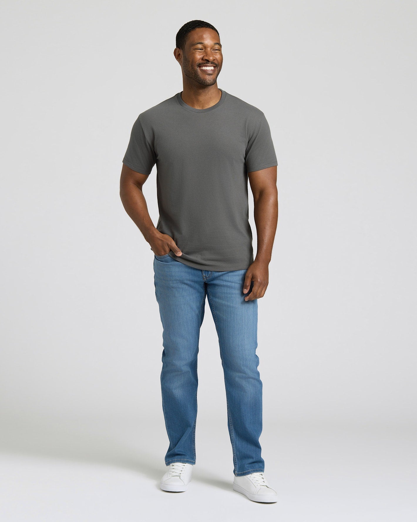 Man wearing a gray t-shirt and blue jeans standing against a plain background. MODEL_INFO: Model is 5'8" wearing size M short