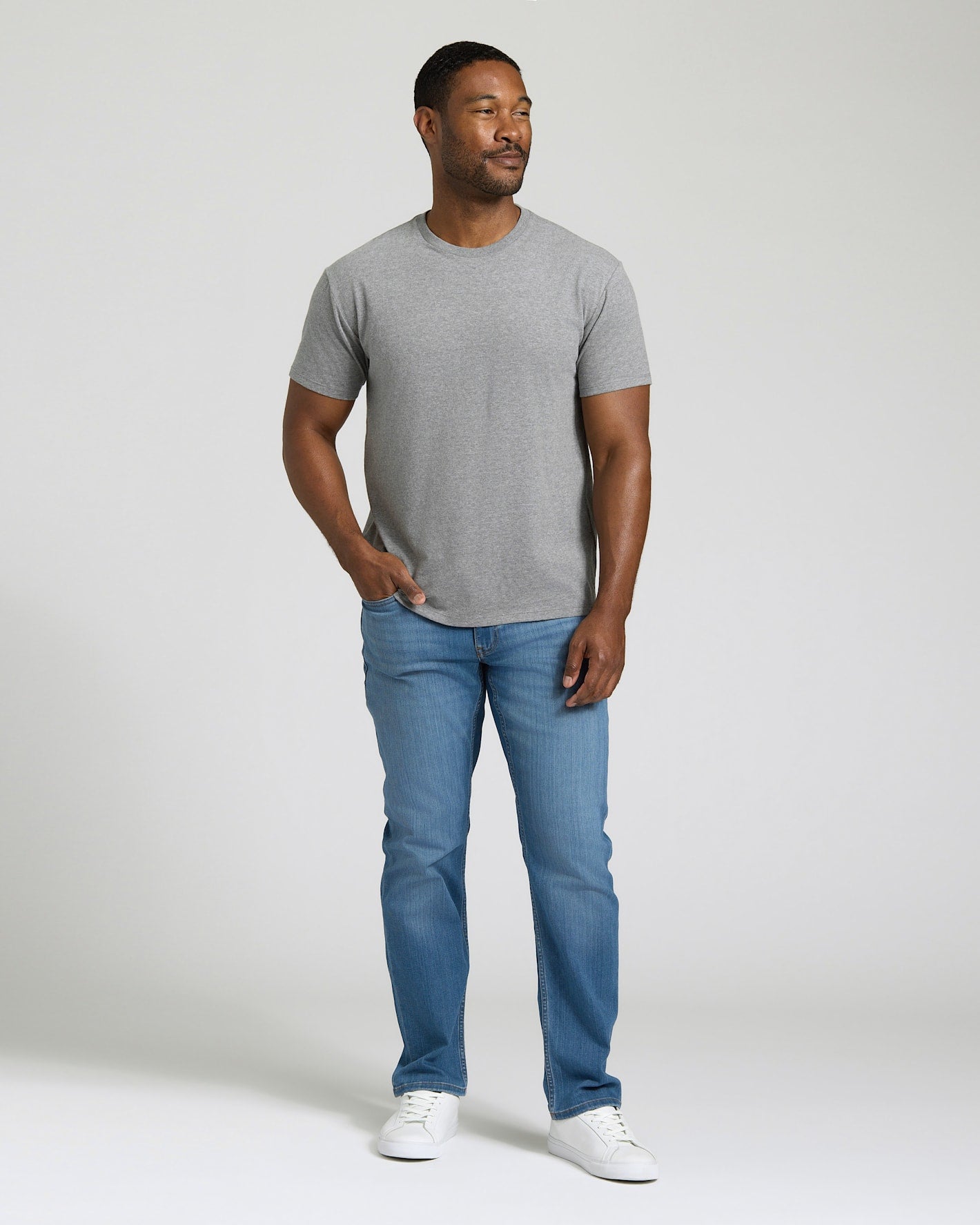 Man wearing a gray t-shirt and blue jeans standing against a plain background. MODEL_INFO: Model is 5'8" wearing size M short