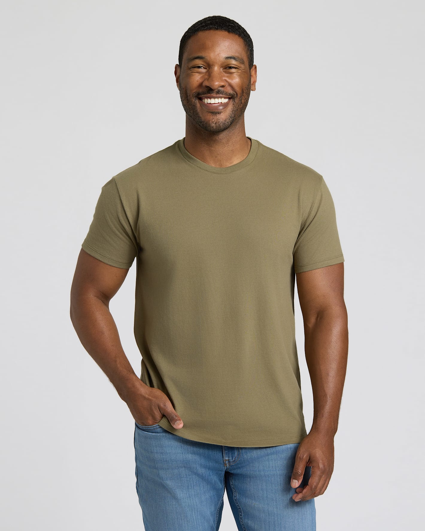 Man wearing an olive green t-shirt and blue jeans against a plain background