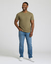 Man wearing a green t-shirt and blue jeans standing against a plain background. MODEL_INFO: Model is 5'8" wearing size M short