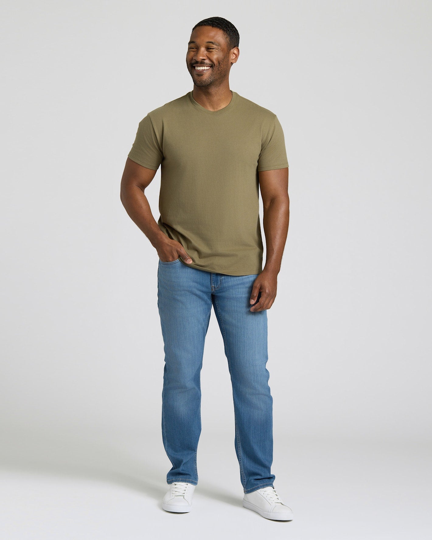 Man wearing a green t-shirt and blue jeans standing against a plain background. MODEL_INFO: Model is 5'8" wearing size M short