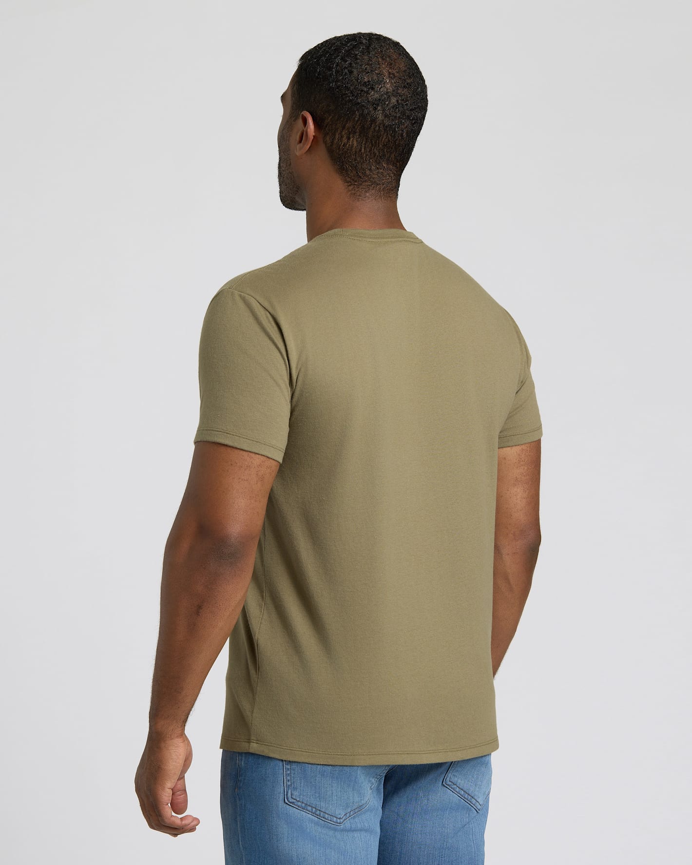 Man wearing a green t-shirt and blue jeans on a plain background