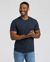 Man wearing a navy blue t-shirt and light blue jeans against a plain background.