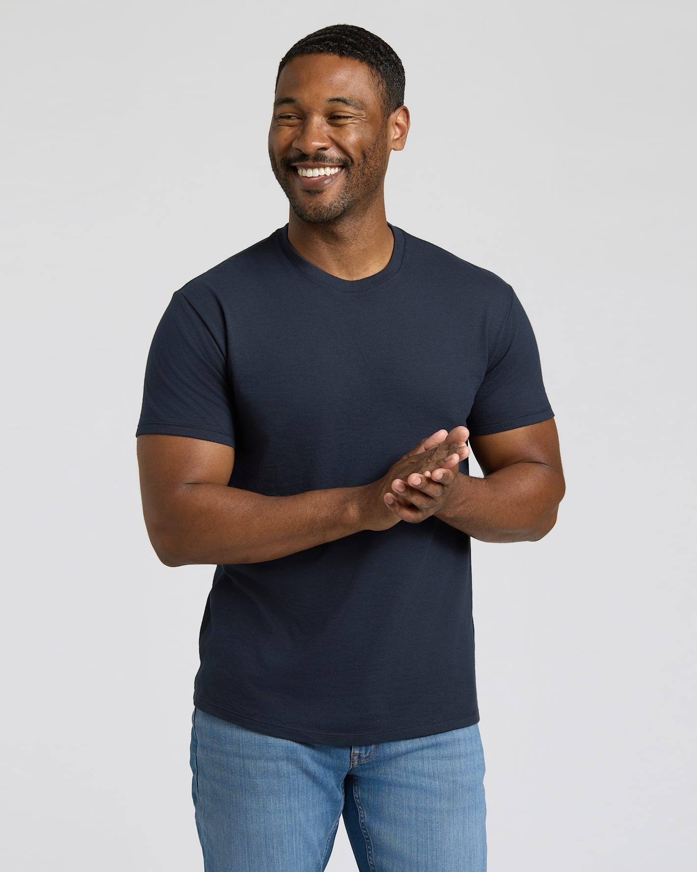 Man wearing a navy blue t-shirt and light blue jeans against a plain background.